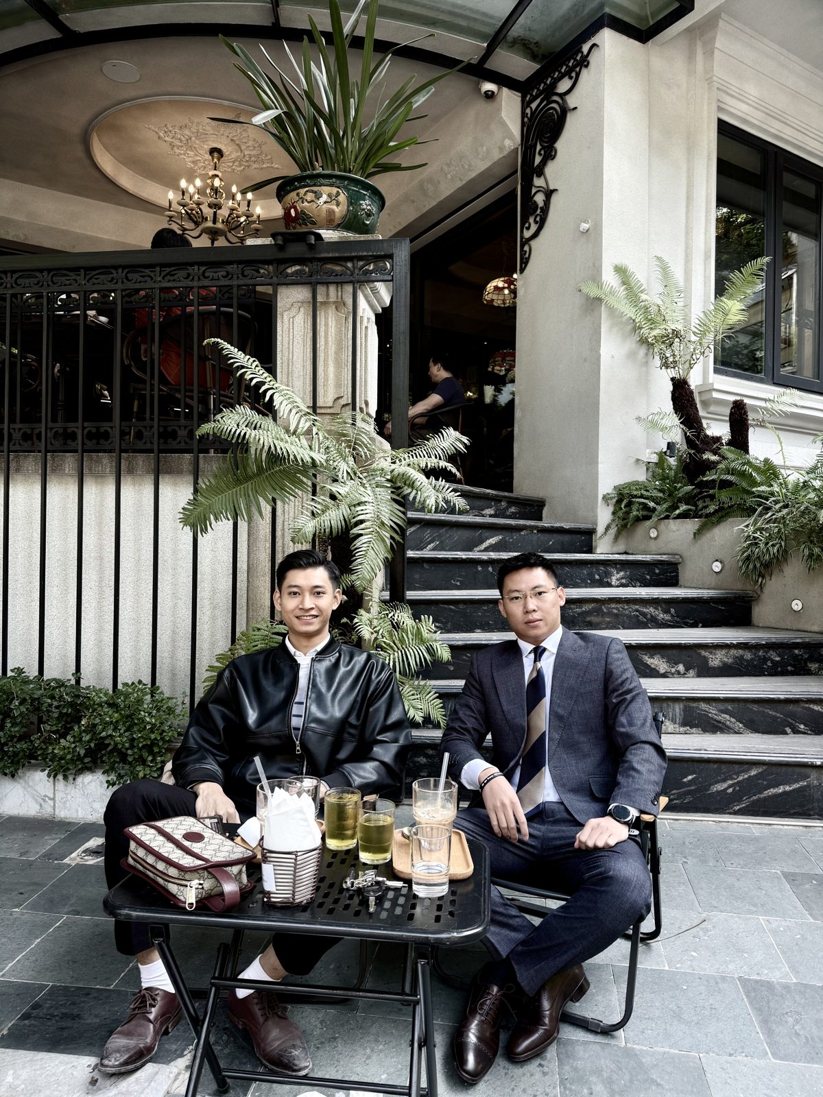 Lê Anh Tuấn mặc vest ngồi trao đổi cùng một người ở quán cà phê sân vườn