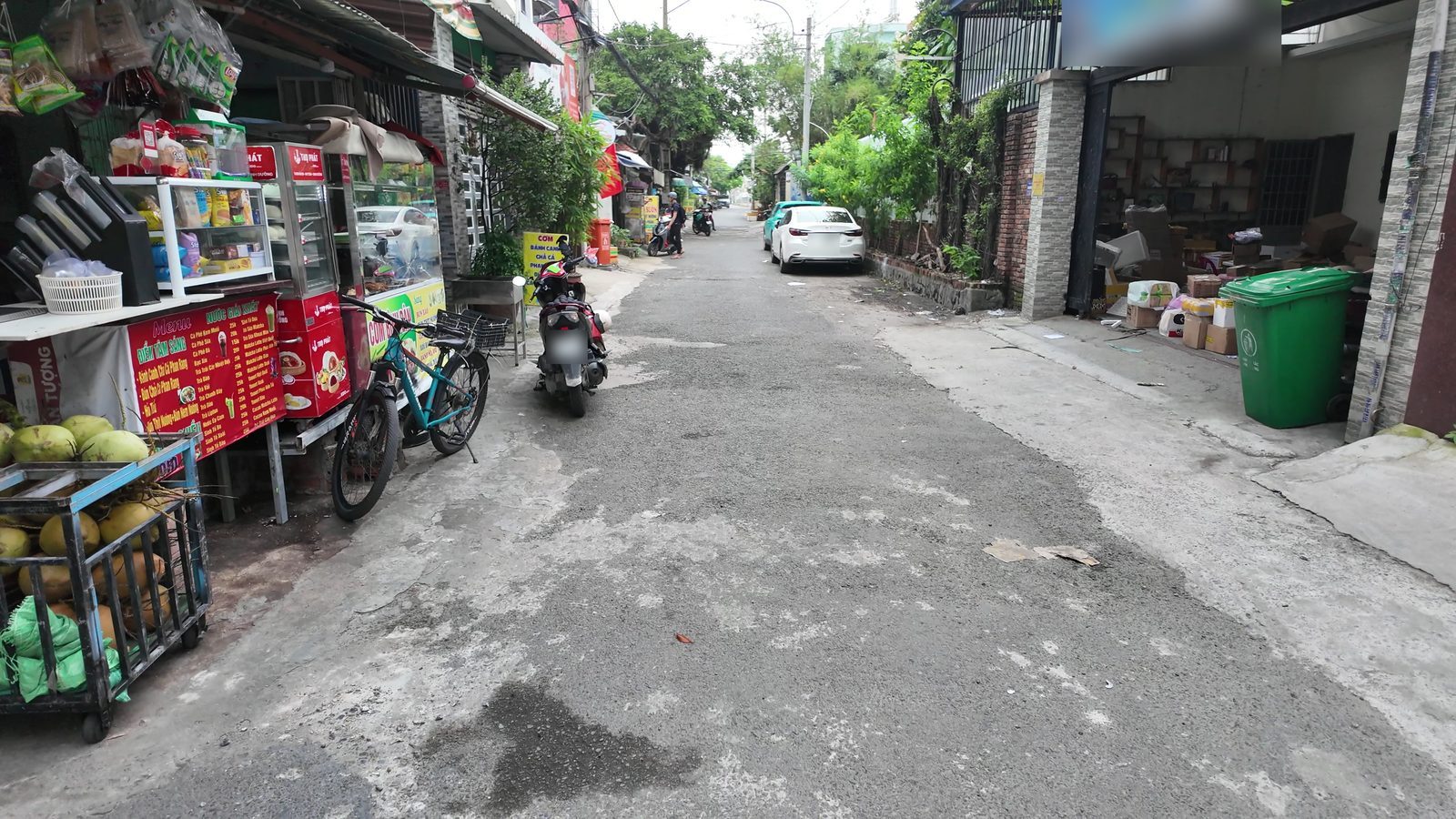 Con đường khu dân cư đông đúc với hàng quán hai bên và xe máy qua lại