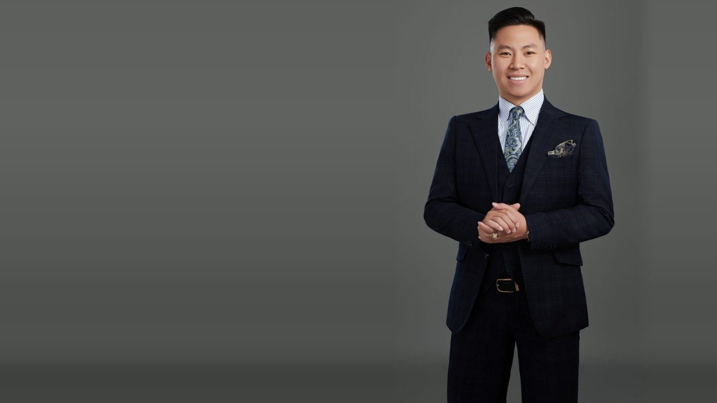 Chân dung Lê Anh Tuấn mặc vest, đứng đan tay trên nền xám