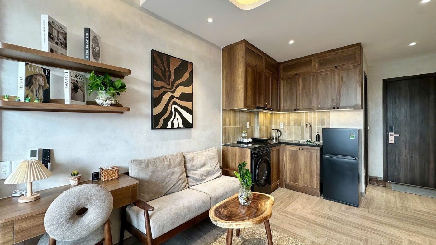 Phòng căn hộ dịch vụ có sofa, bàn làm việc, kệ gỗ và góc bếp