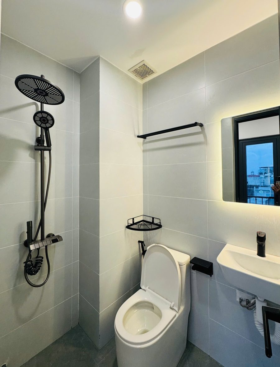 Phòng tắm ốp gạch sáng, sen tắm, bồn cầu và gương đèn