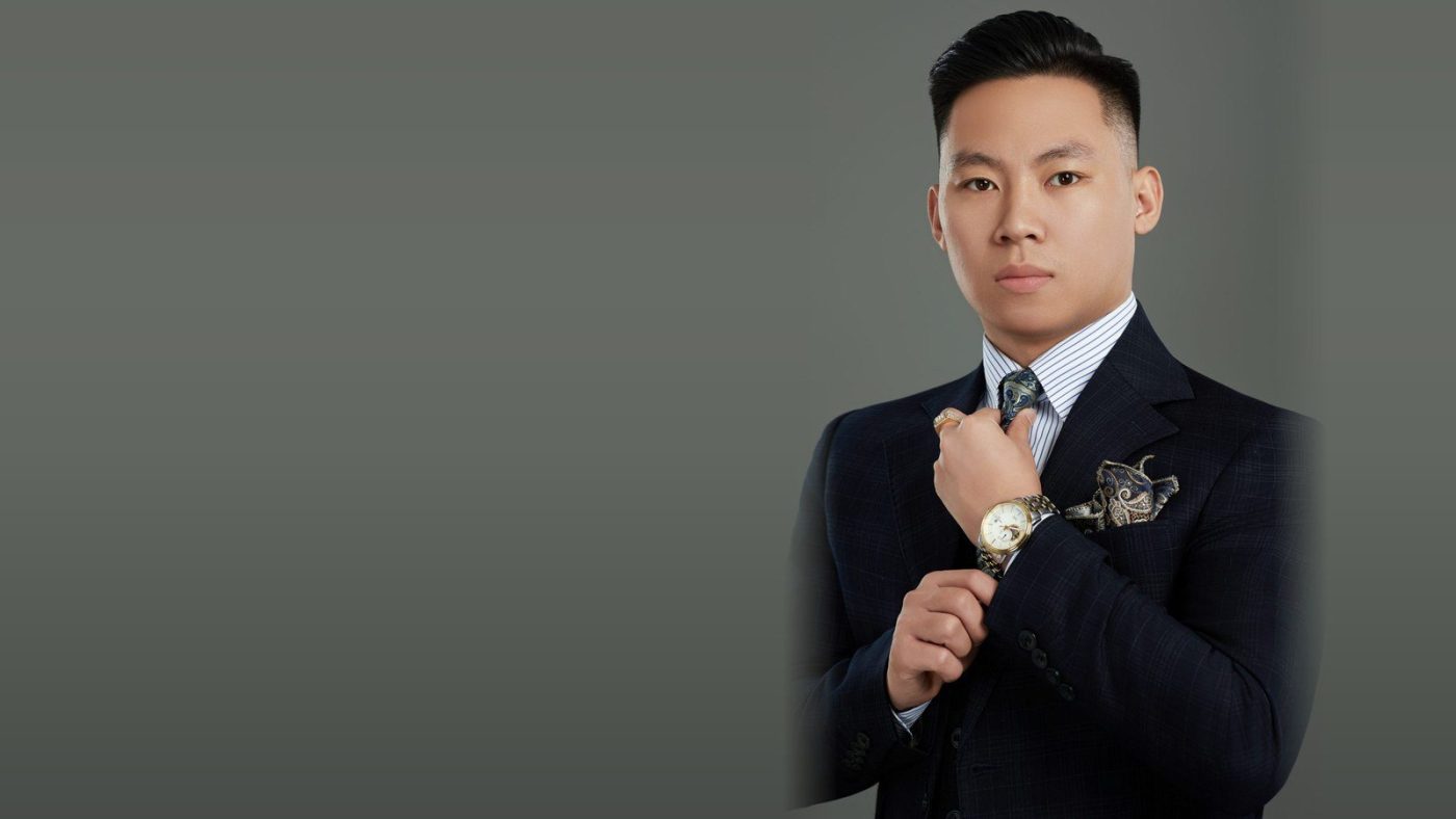 Chân dung Lê Anh Tuấn mặc vest, chỉnh cổ tay áo trên nền xám