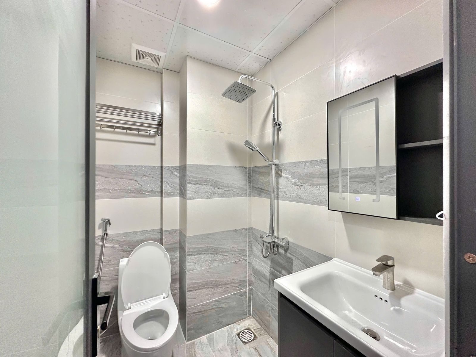 Nhà tắm ốp gạch sáng màu có vòi sen, bồn cầu, lavabo và phễu thoát sàn