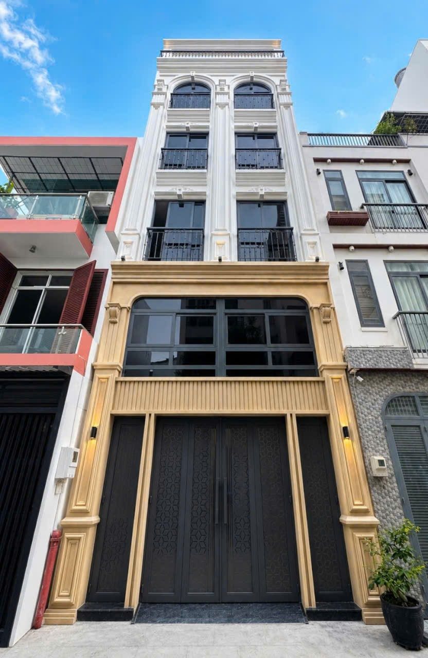 Tòa nhà năm tầng mặt tiền kem và vàng có cửa sắt lớn, nằm giữa các nhà phố
