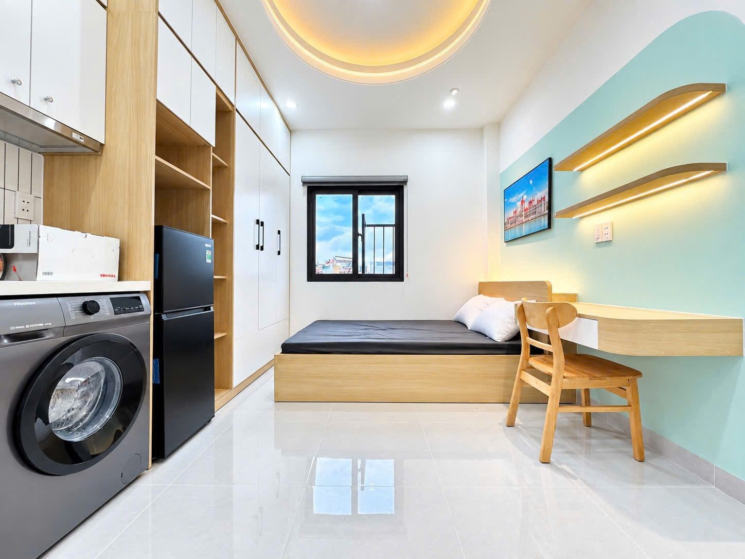 Phòng cho thuê có giường bệ gỗ, bàn học, máy giặt, tủ lạnh và tủ bếp trắng, tường xanh nhạt