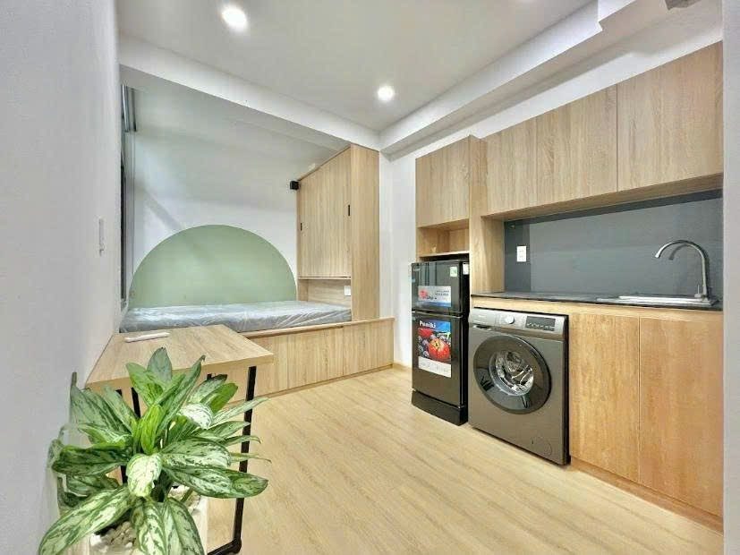 Phòng có gác lửng, cầu thang kiêm tủ, tủ lạnh nhỏ, bàn làm việc và cửa kính ra ban công
