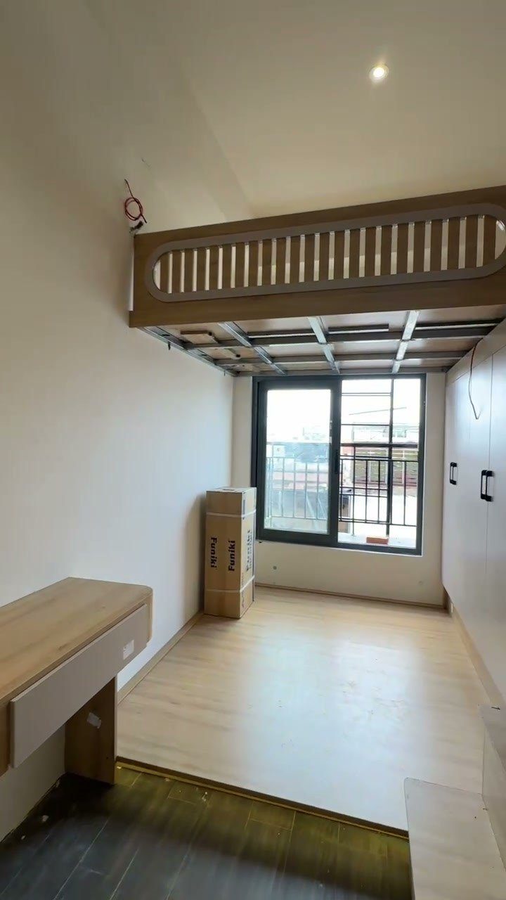 Phòng có gác lửng gỗ, ô cửa sổ nhìn ra đường và bệ gỗ cạnh cửa, tường trắng