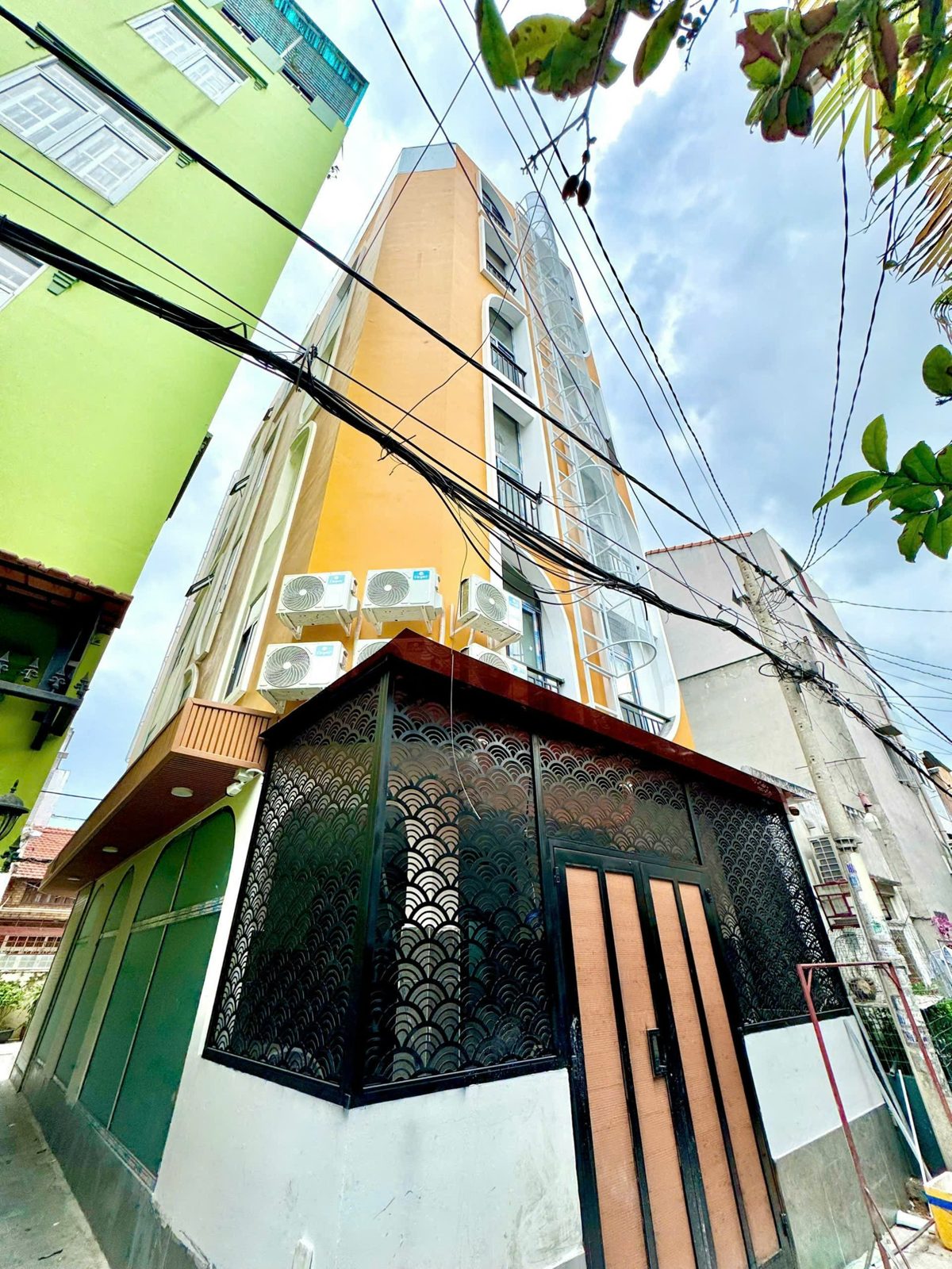 Góc một tòa nhà nhiều tầng sơn cam trong hẻm, tầng trệt có khung sắt hoa văn và cửa gỗ