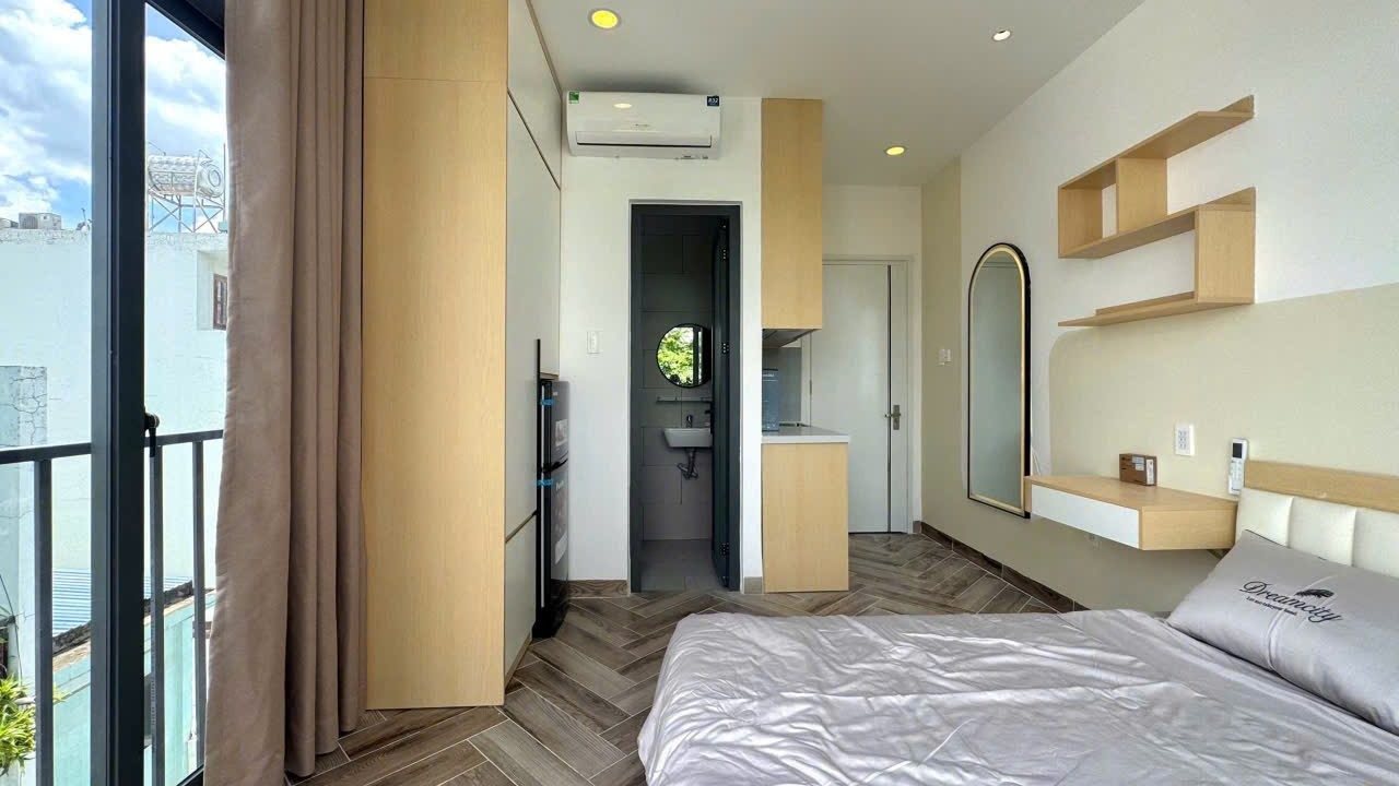Phòng cho thuê có giường, kệ gỗ trên tường và cửa kính ra ban công, ảnh bìa bài viết về bán nhà bằng giá mua vào