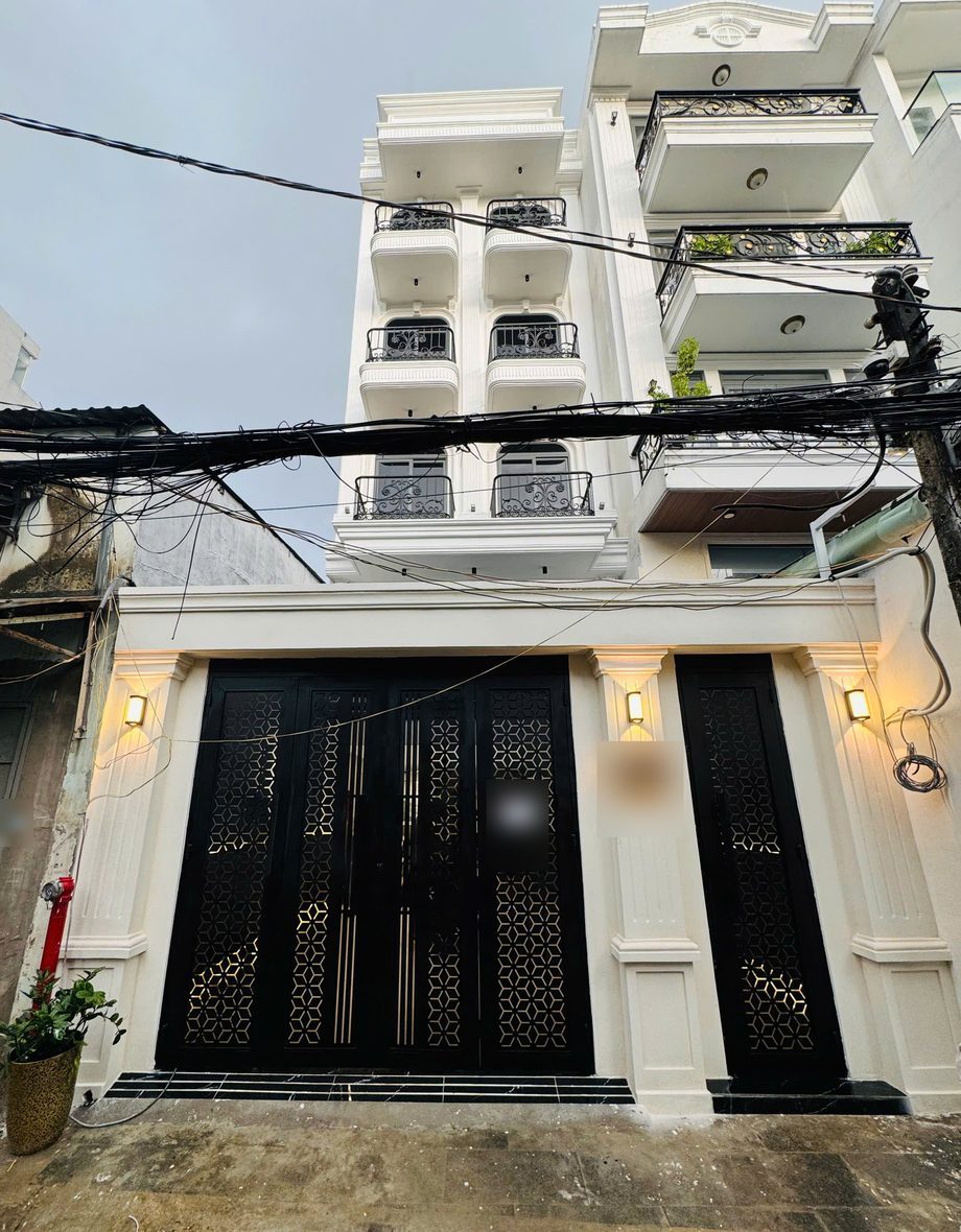 Mặt tiền một tòa nhà năm tầng sơn trắng có cổng sắt đen và đèn tường, nhìn từ dưới hẻm