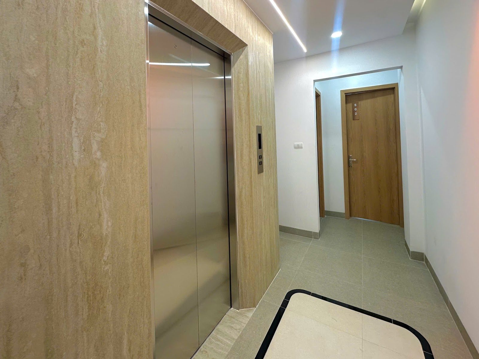 Cửa thang máy inox ở hành lang lát gạch xám của một tòa nhà cho thuê