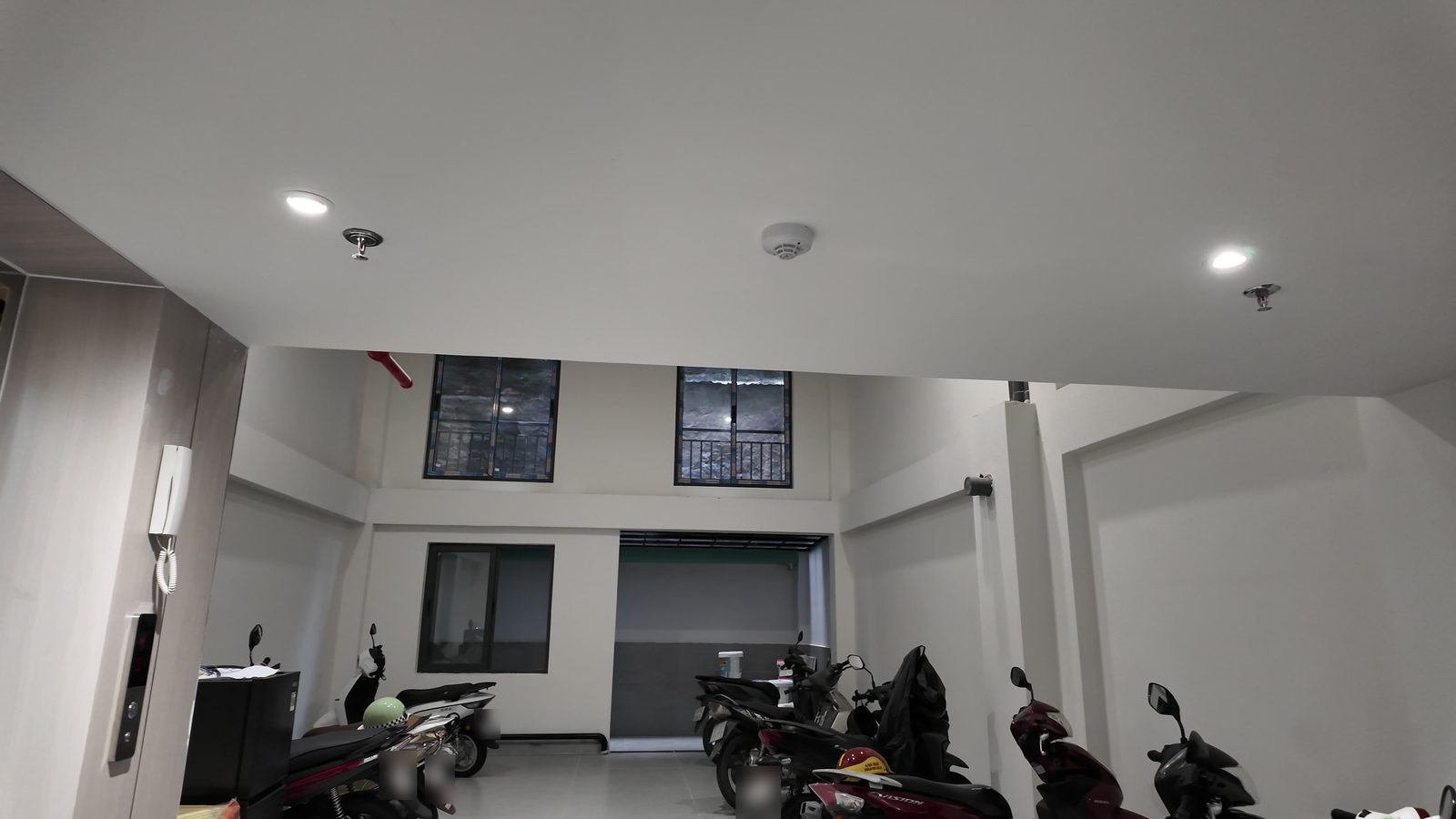 Sảnh tầng trệt một tòa nhà cho thuê dùng làm chỗ để xe máy, trần cao, có đèn âm trần và chuông cửa có hình