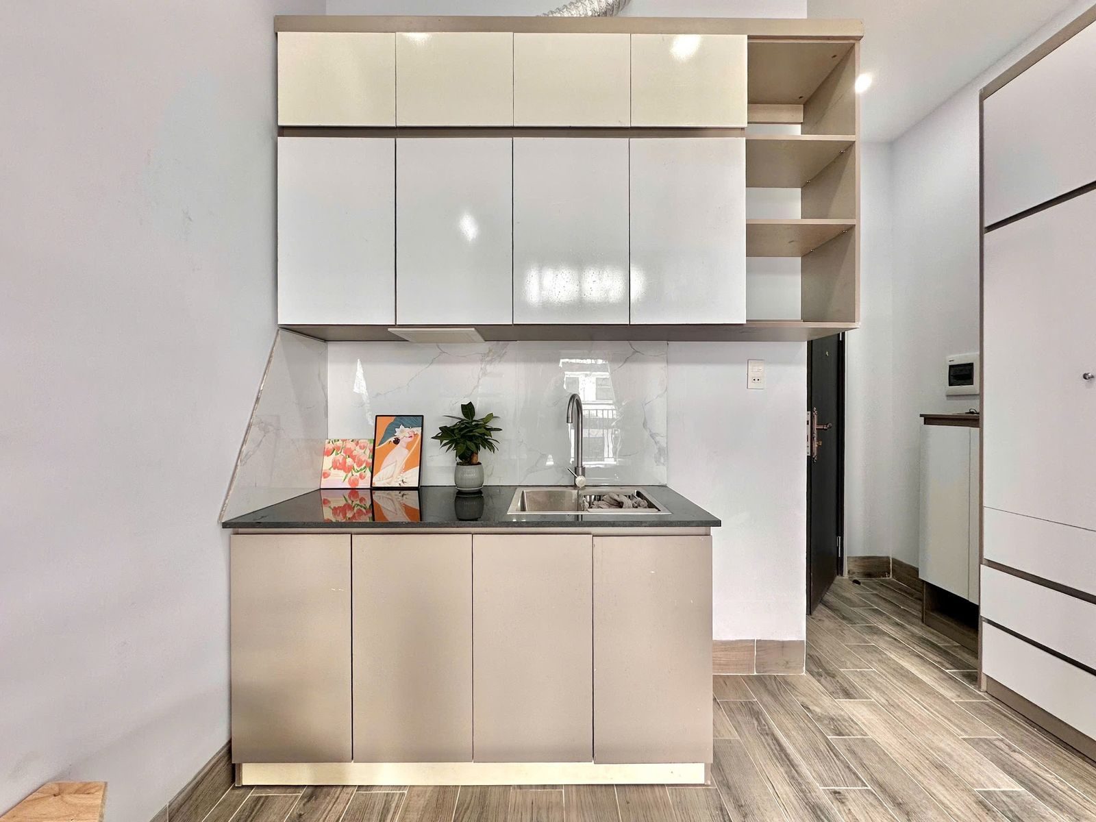 Tủ bếp trắng có bồn rửa và kệ trang trí trong một phòng cho thuê