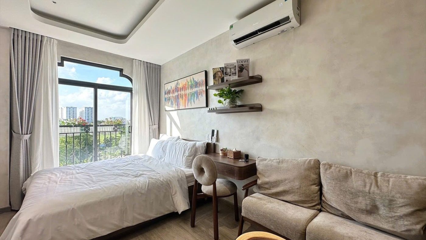 Phòng ngủ có giường, bàn nhỏ, sofa và cửa sổ lớn nhìn ra thành phố, ảnh bìa bài viết về căn hộ dịch vụ có bán được không