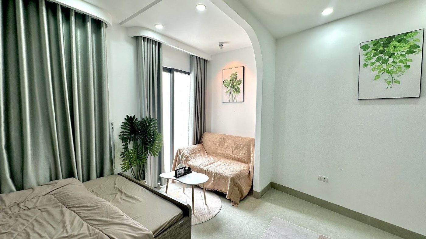 Phòng cho thuê sáng có giường, ghế sofa nhỏ và rèm cửa xanh ngả, ảnh bìa bài viết về căn hộ dịch vụ Gò Vấp Tân Bình Bình Thạnh