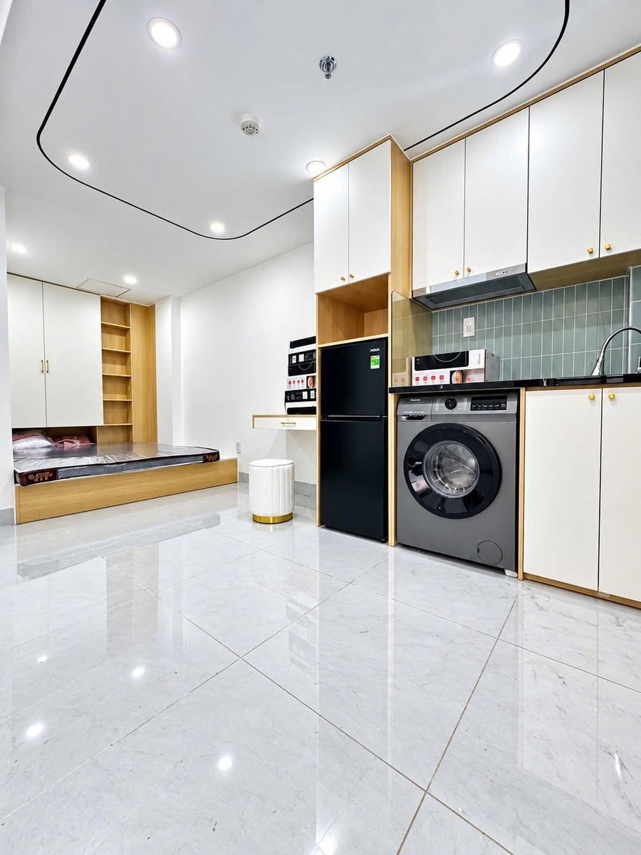 Phòng studio sàn gạch trắng có giường, tủ lạnh, máy giặt, bếp và tủ treo màu trắng
