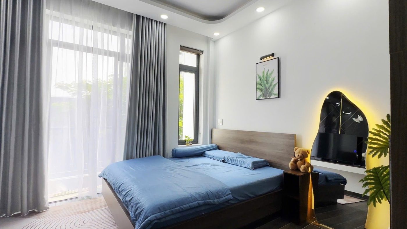 Phòng ngủ có giường ga xanh, rèm cửa lớn và gương viền đèn, ảnh bìa bài viết về cần tiền gấp khi giữ nhà cho thuê