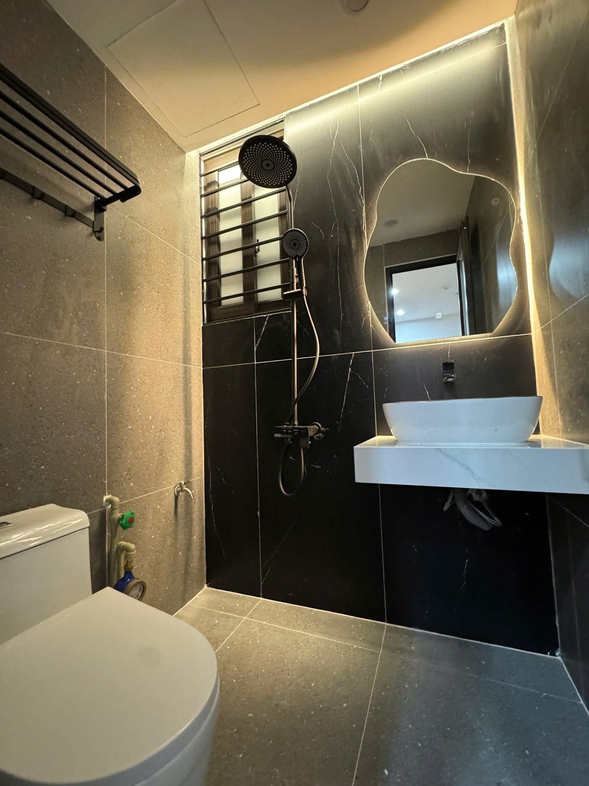 Nhà tắm phòng cho thuê ốp đá tối màu có gương viền đèn, sen cây và lavabo đặt bàn