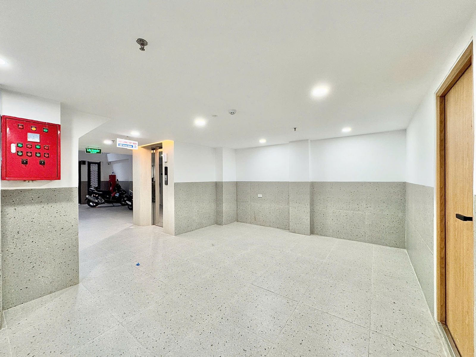 Tầng trệt một tòa nhà cho thuê có tủ điều khiển báo cháy màu đỏ trên tường, thang máy và khu để xe phía trong