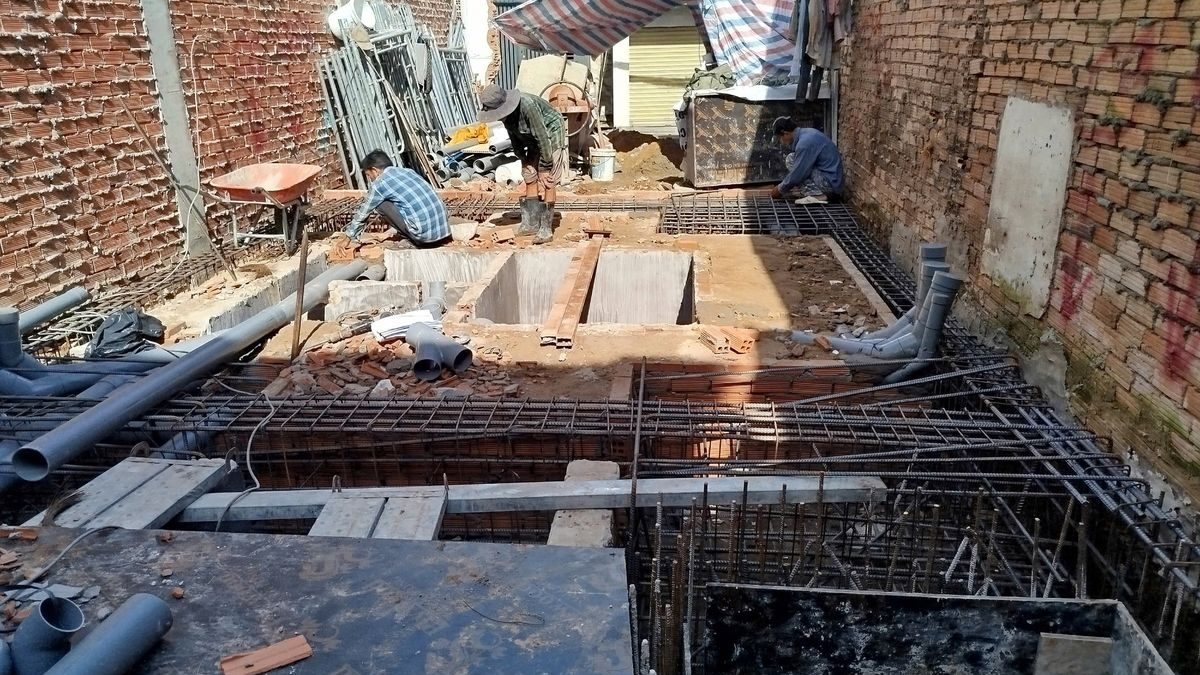 Công trường làm móng một tòa nhà giữa hai bức tường gạch, thợ đang đan thép, ảnh bìa bài viết về chi phí xây căn hộ dịch vụ