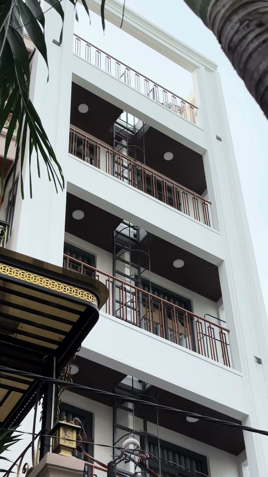 Mặt tiền tòa nhà trắng nhiều tầng có ban công gỗ nhìn từ dưới lên