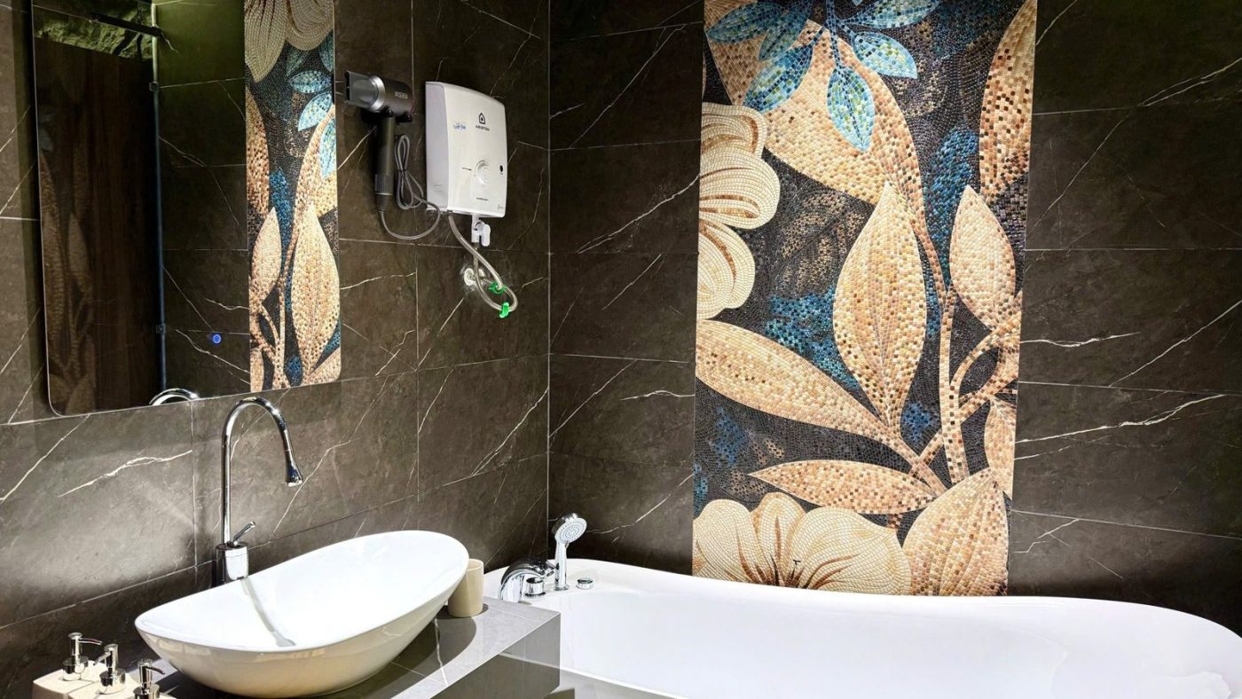 Phòng tắm ốp đá tối màu có bồn tắm nằm, lavabo đặt bàn và mảng tường tranh hoa