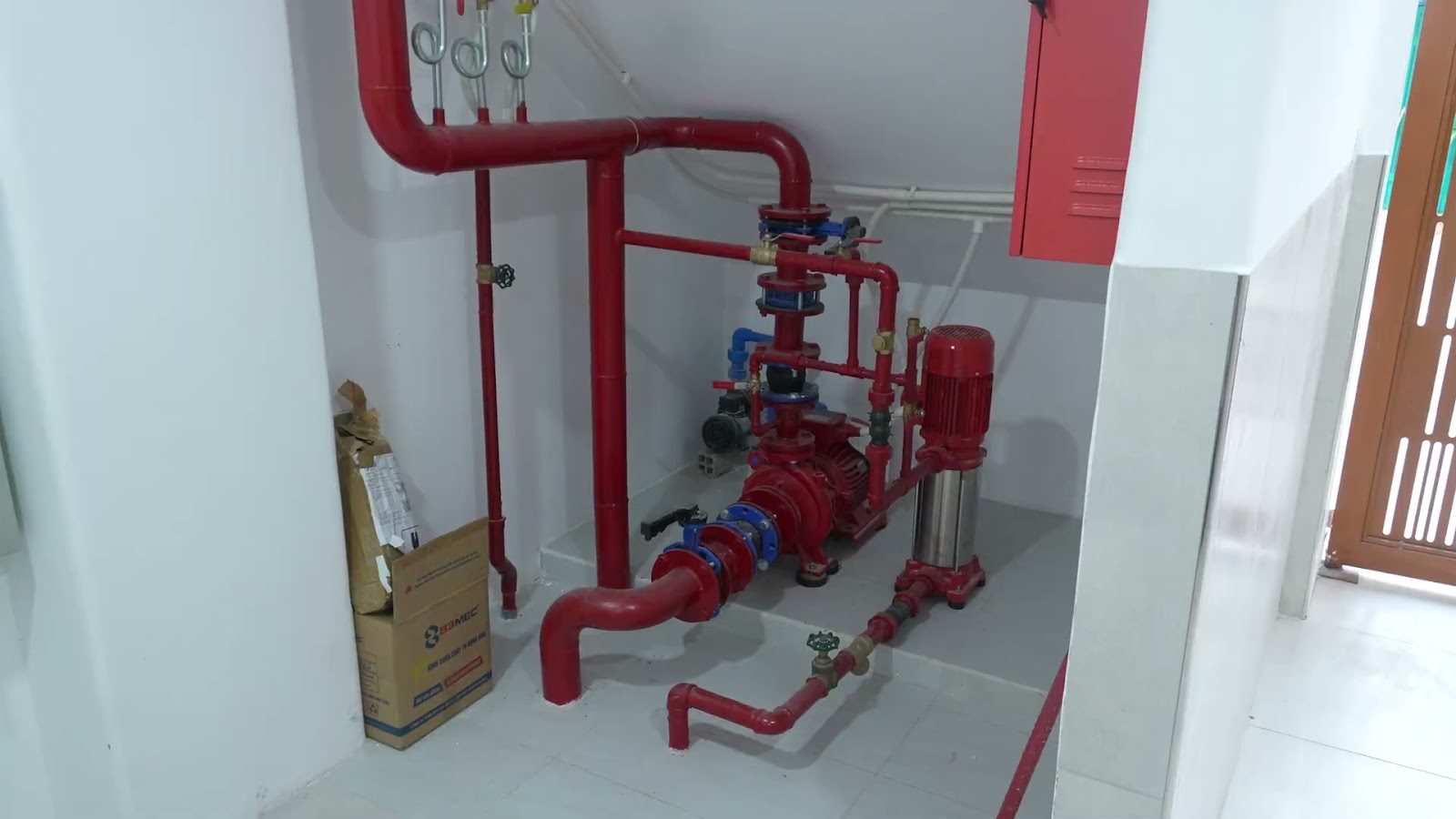 Đường ống và máy bơm chữa cháy sơn đỏ đặt ở góc tầng trệt