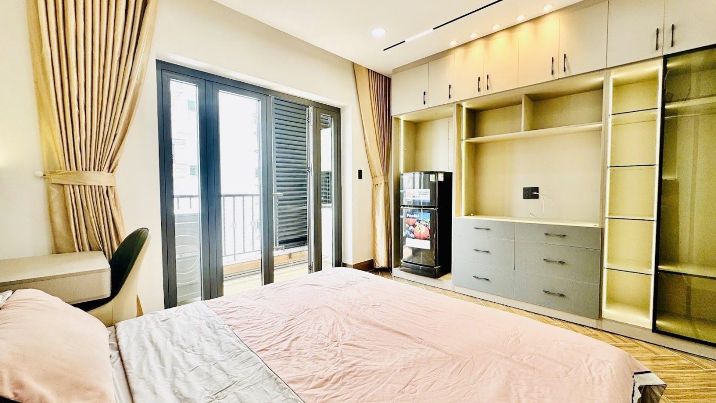 Phòng cho thuê có giường ga hồng, kệ gỗ kín tường và cửa ra ban công, ảnh bìa bài viết về chủ nhà bán vì áp lực lãi vay