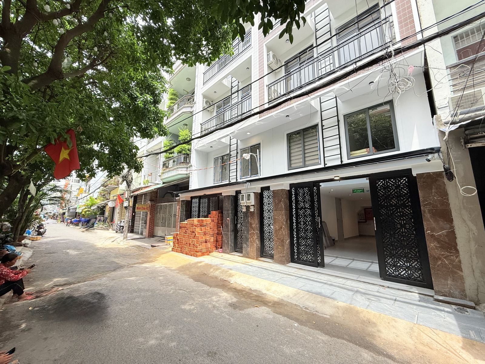 Dãy nhà phố mới xây trên một con đường nhỏ rợp cây, tầng trệt còn để trống, có đống gạch trước cửa