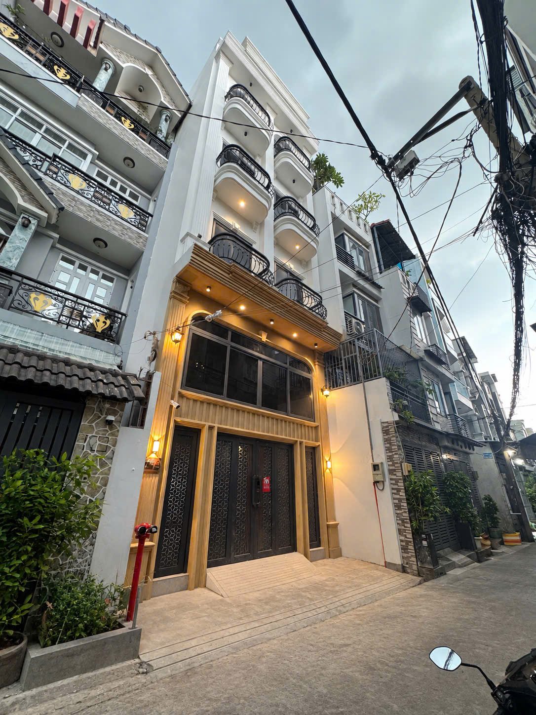 Mặt tiền một tòa nhà cho thuê nhiều tầng trong hẻm lúc chiều tối, cửa sắt hoa văn, đèn tường đã bật và ban công từng tầng