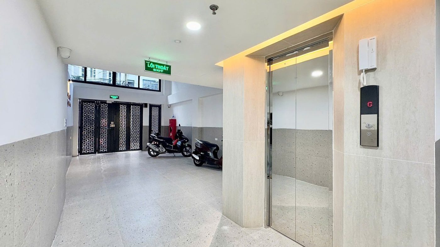Sảnh tầng trệt một tòa nhà cho thuê có thang máy, bảng điều khiển trên tường và xe máy đỗ phía trong, ảnh bìa bài viết về giao tiền trước hay công chứng trước