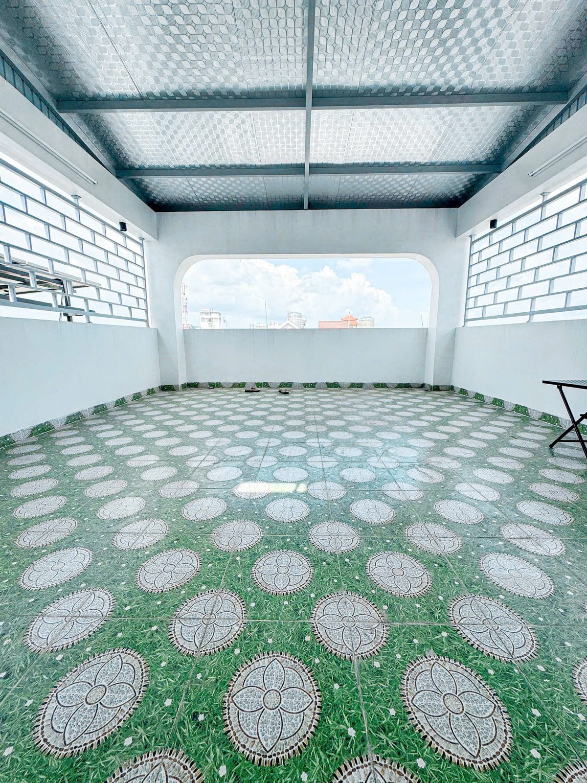 Sân thượng lát gạch hoa xanh trắng có giàn lưới che và ô cửa sổ vòm