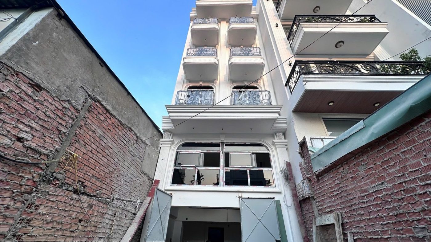 Dãy nhà phố năm tầng sơn trắng nhìn từ một lô đất đang xây trong hẻm, ảnh bìa bài viết về hẻm bao nhiêu mét được xây mấy tầng