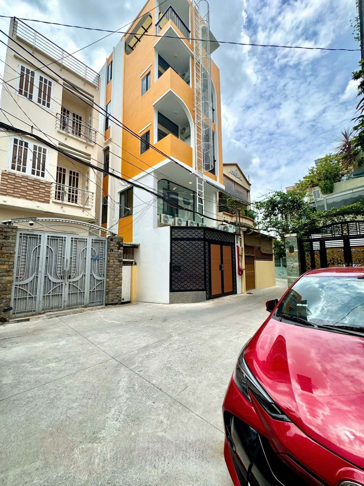 Con hẻm bê tông rộng trước một tòa nhà cho thuê, có ô tô đỗ ven đường