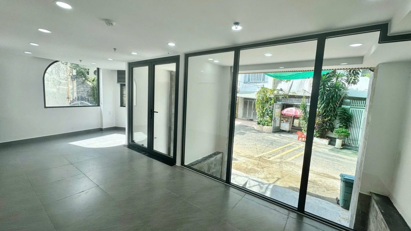 Tầng trệt rộng lát gạch xám với cửa kính lớn nhìn ra con hẻm có bãi đỗ, ảnh bìa bài viết về hẻm xe hơi và hẻm xe máy