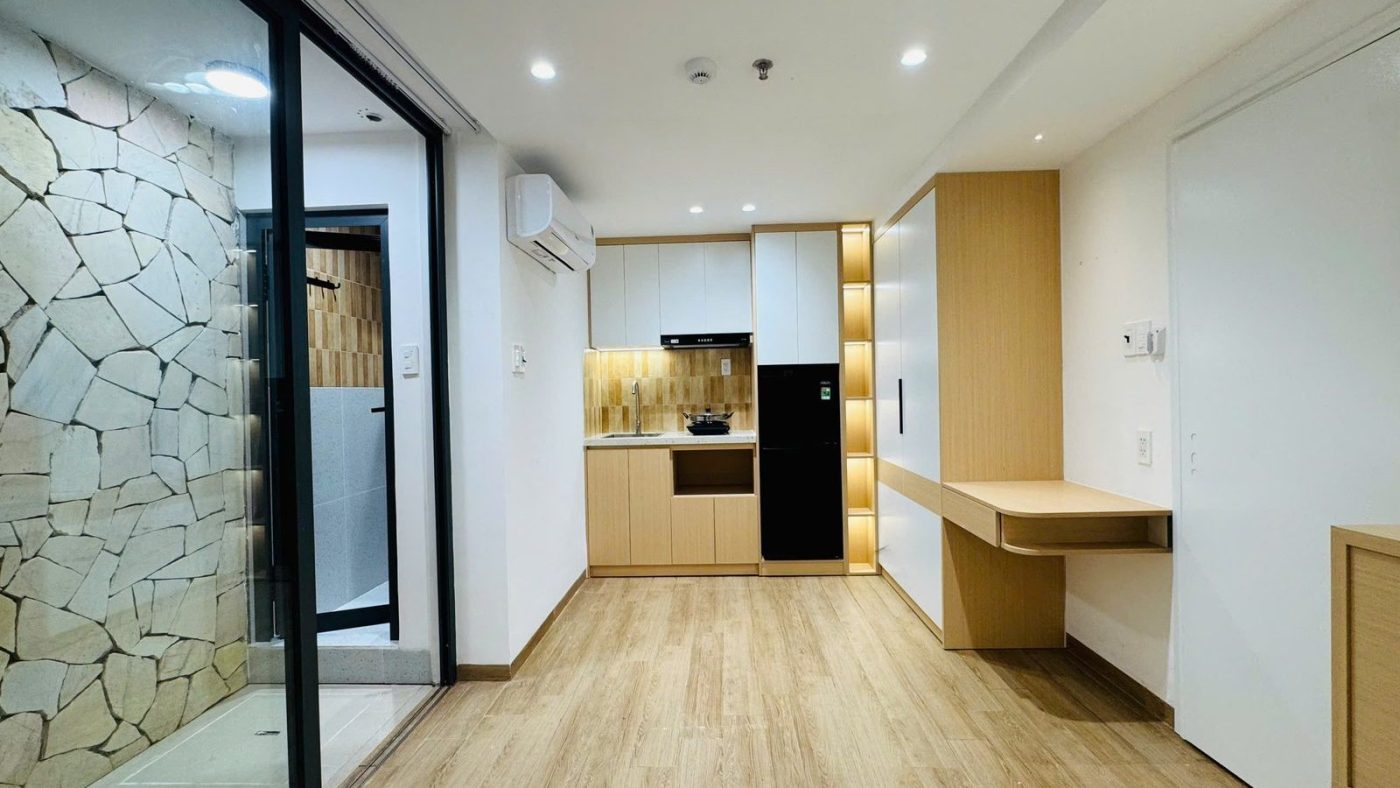 Phòng cho thuê có mảng tường ốp đá, vách kính, bếp gỗ sáng và bàn làm việc
