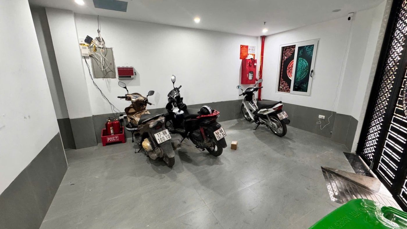 Tầng trệt để xe của một tòa nhà cho thuê có ba xe máy, bình chữa cháy và tủ điện trên tường, ảnh bìa bài viết về kiểm chứng lời môi giới