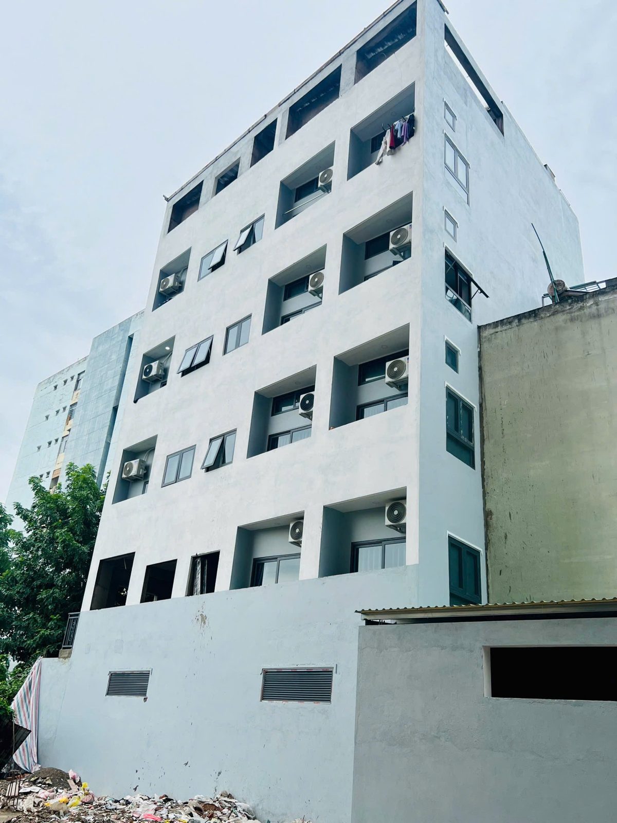 Tòa nhà cho thuê nhiều tầng sơn trắng nhìn từ phía sau, mỗi tầng có cục nóng điều hòa
