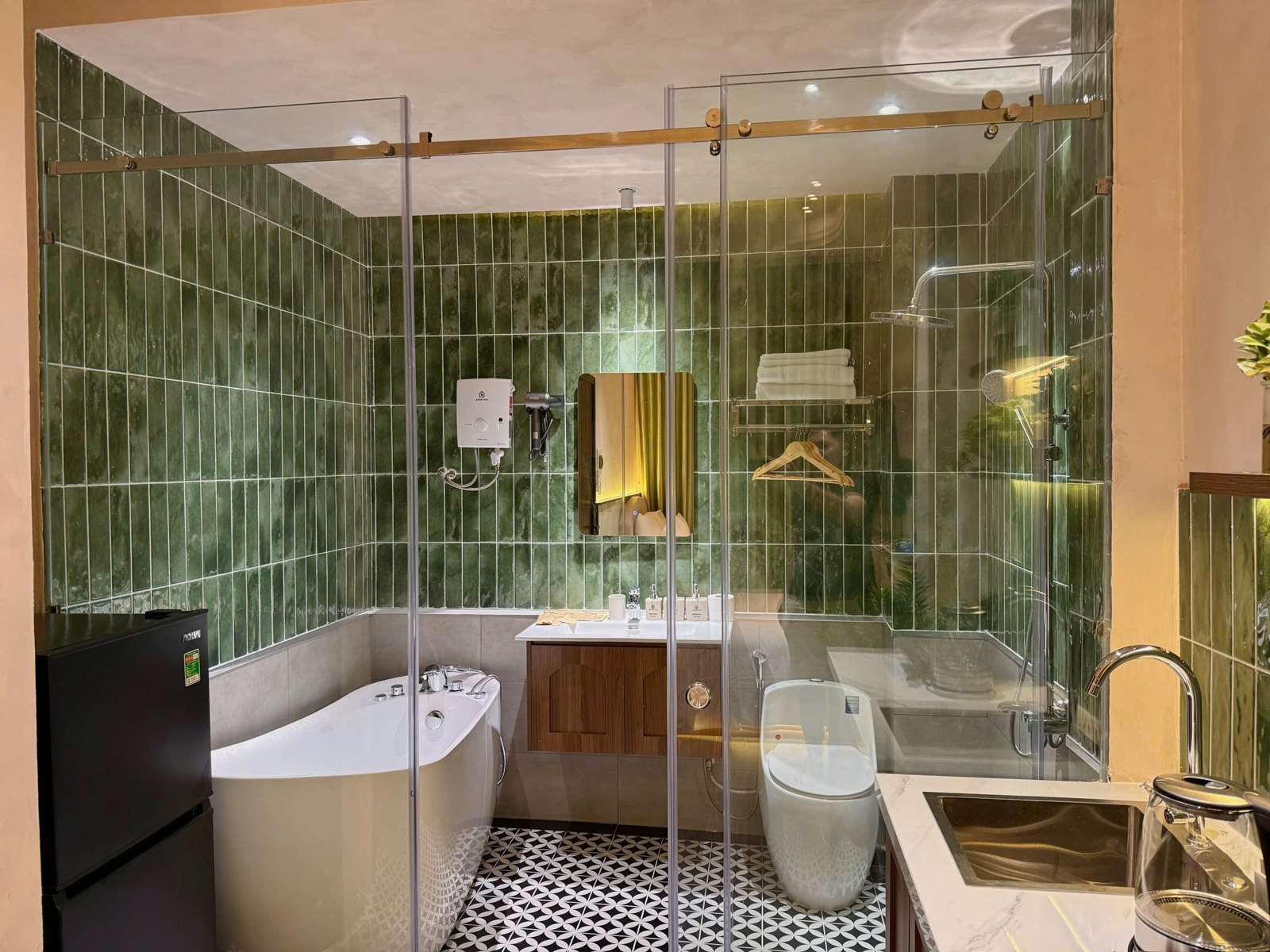 Nhà tắm vách kính ốp gạch xanh có bồn tắm, lavabo và bồn cầu