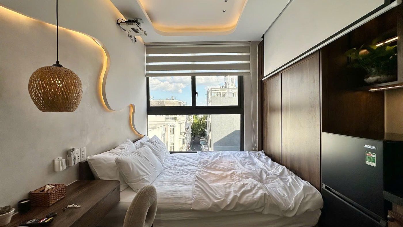 Phòng cho thuê có đèn thả mây, giường cạnh cửa sổ rèm cuốn, tủ lạnh và tường ốp gỗ, ảnh bìa bài viết về mỗi môi giới báo một giá