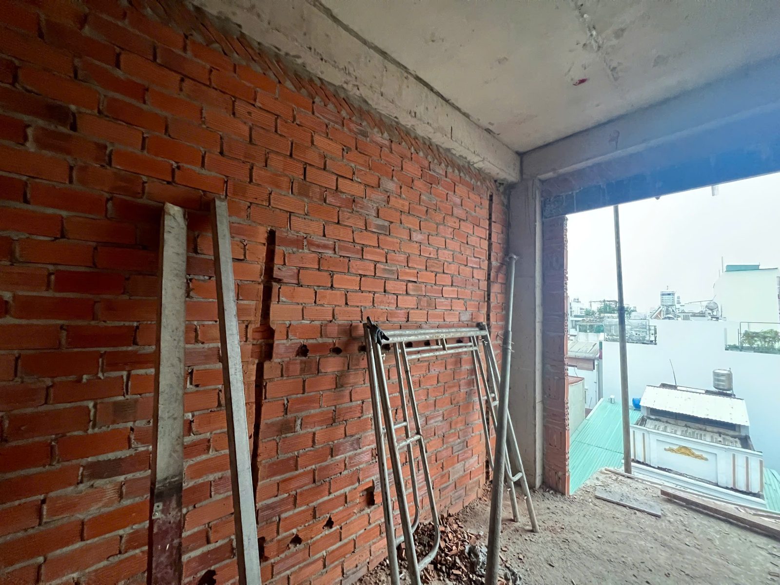 Một tầng đang xây có tường gạch, giàn giáo dựng sát tường và ô cửa nhìn ra khu dân cư