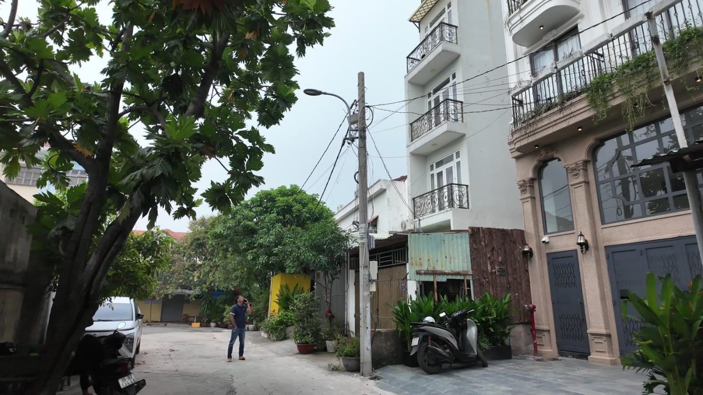 Đường hẻm ô tô rợp bóng cây ở Gò Vấp, bên phải là một tòa nhà cho thuê màu trắng