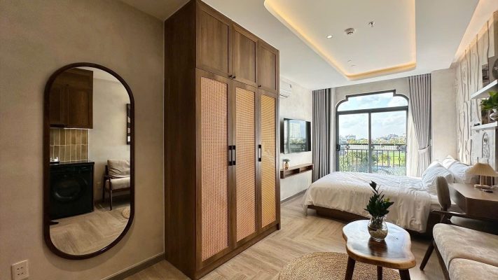 Phòng cho thuê có gương bầu dục, tủ áo gỗ cánh mây, giường và cửa sổ vòm nhìn ra thành phố