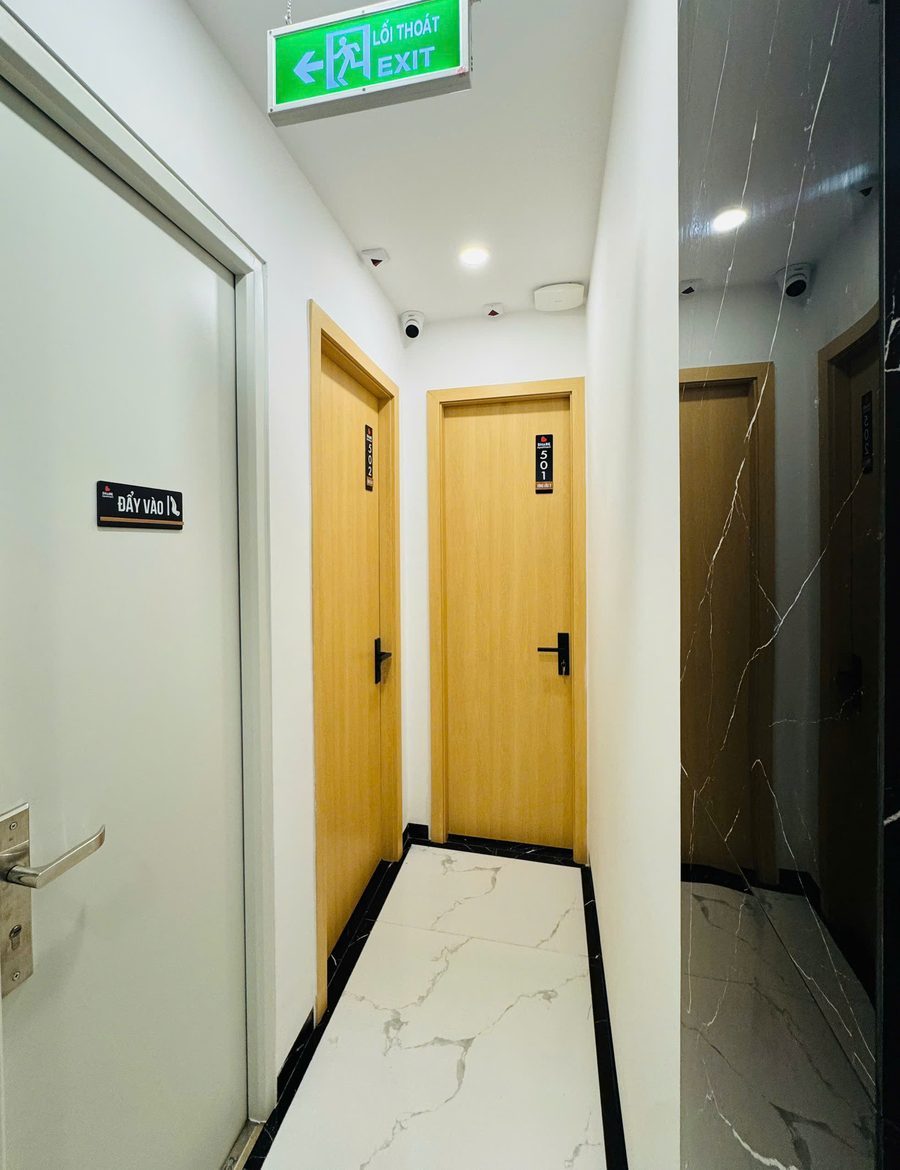 Hành lang tòa nhà cho thuê có các cửa phòng bằng gỗ và đèn chỉ lối thoát hiểm