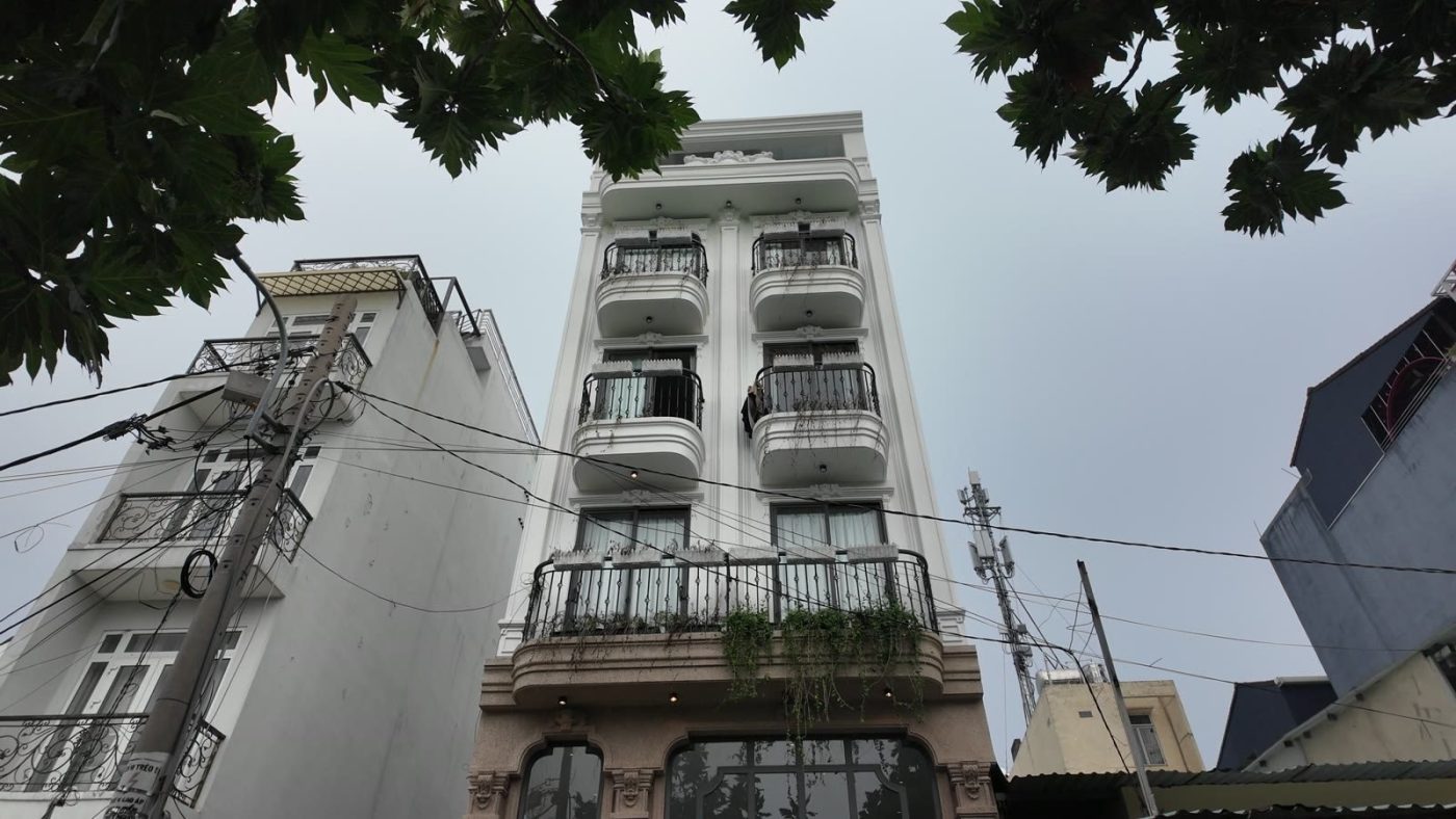 Mặt tiền tòa nhà cho thuê kiểu tân cổ điển màu trắng nhìn từ dưới lên, có ban công sắt và cây xanh