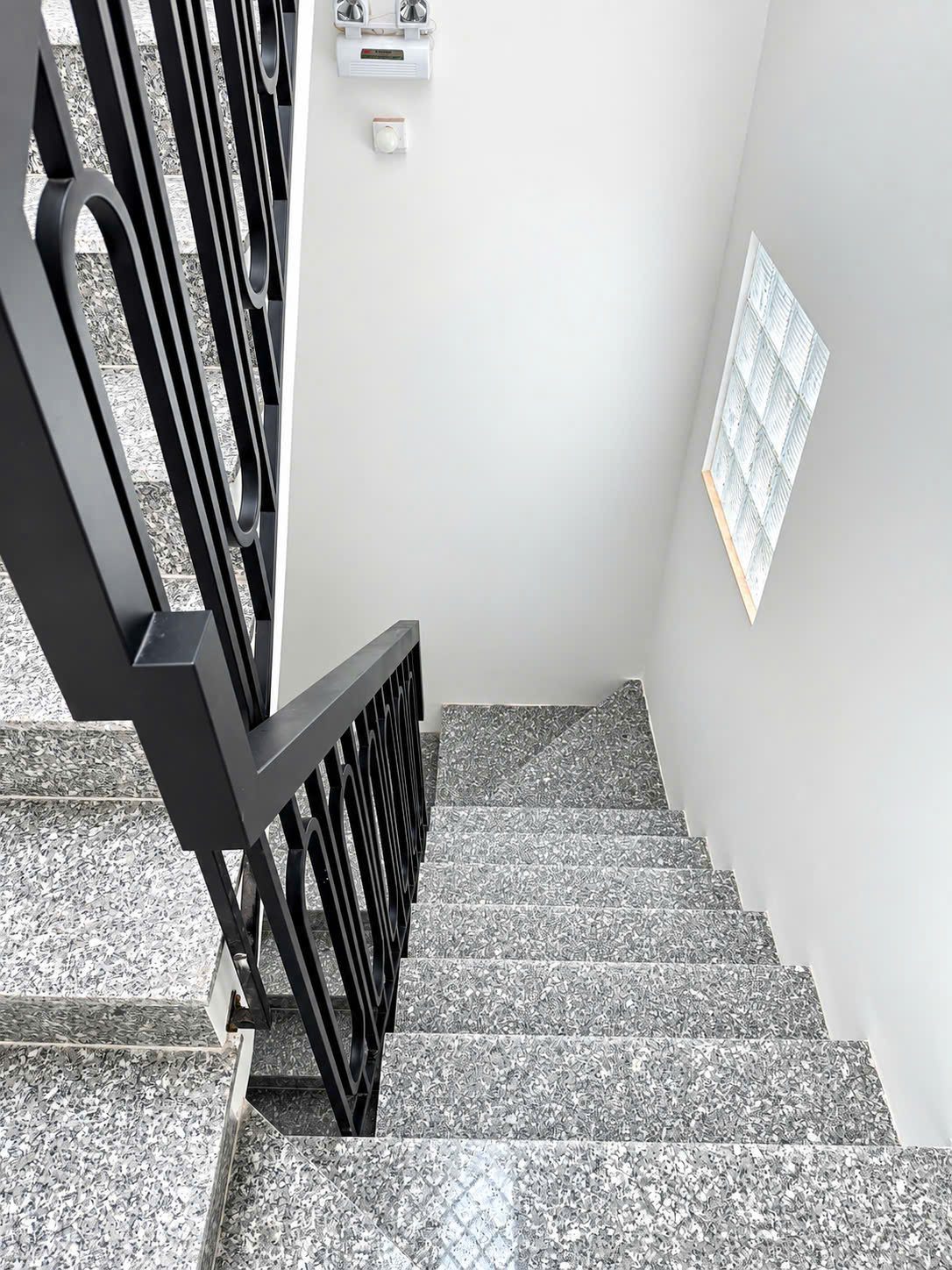 Cầu thang đá granite có lan can sắt đen và ô gạch kính lấy sáng