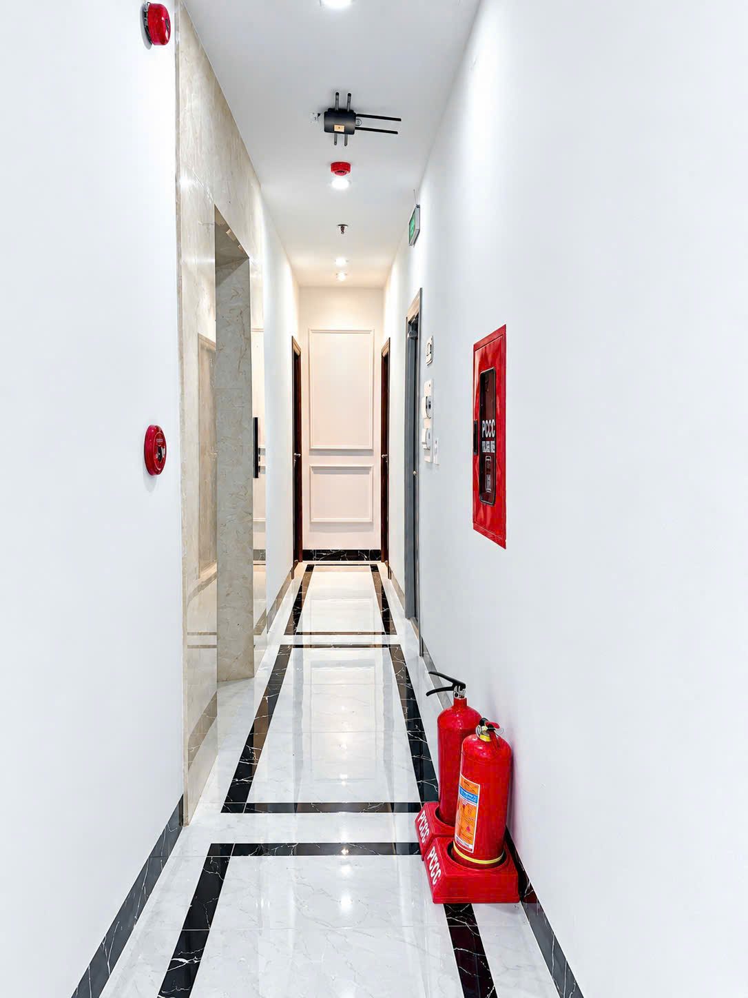 Hành lang một tòa nhà cho thuê có bình chữa cháy, chuông báo cháy và tủ vòi chữa cháy trên tường