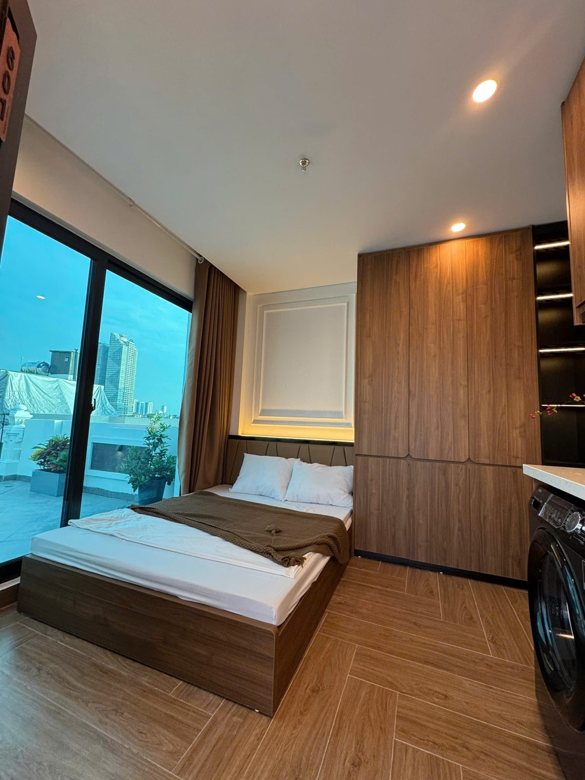 Phòng ngủ cho thuê có giường đôi, tủ gỗ và cửa kính lớn nhìn ra thành phố
