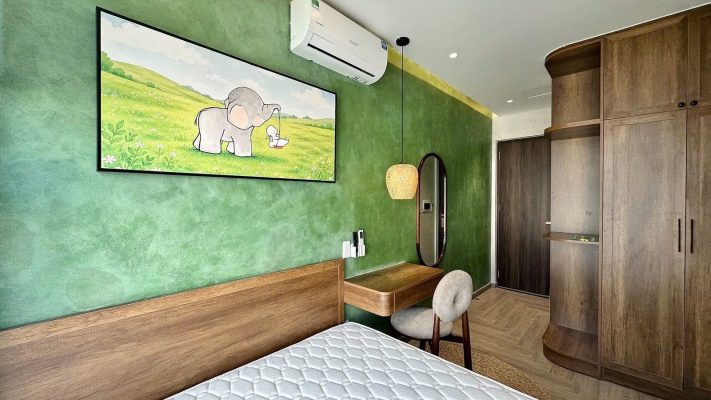 Phòng cho thuê có mảng tường xanh treo tranh chú voi, giường gỗ, bàn làm việc và tủ áo