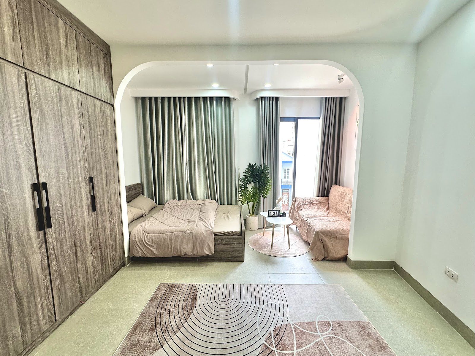 Phòng ngủ có giường, ghế sofa nhỏ, tủ gỗ lớn và rèm cửa xanh xám